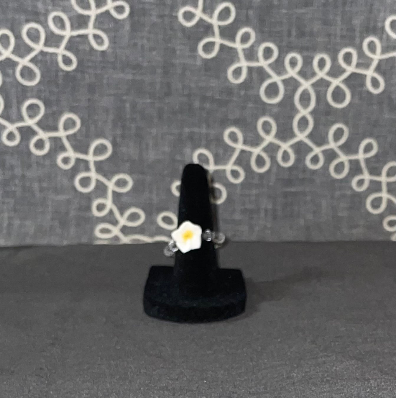 Handmade white daisy ring with clear sparkle bead accents on a black ring display stand