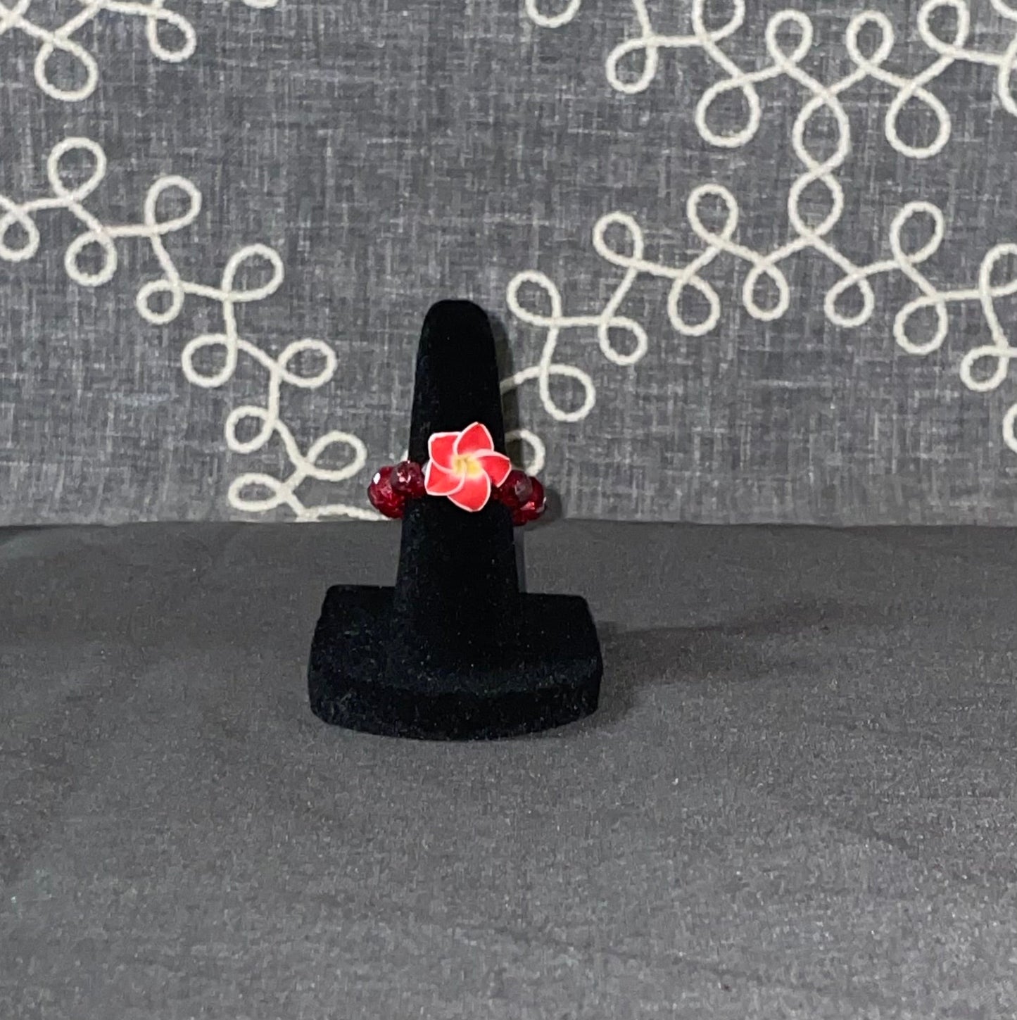 Crimson Plumeria Bloom Ring with deep red beads and vibrant plumeria flower centerpiece on a black ring display