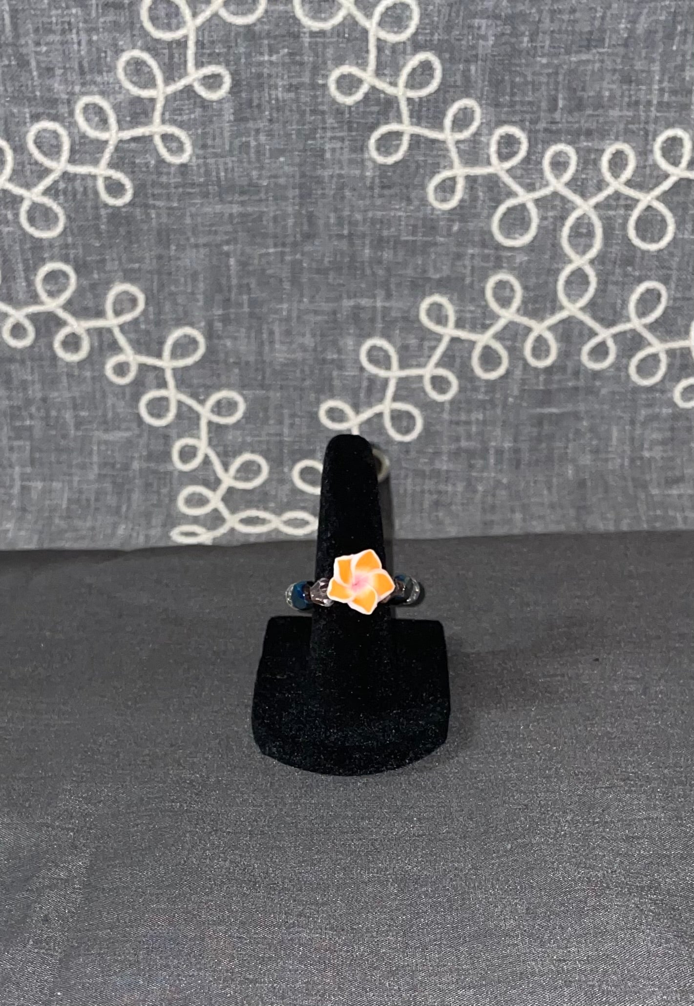 Handmade orange daisy flower ring with blue bead accents on a black ring display stand